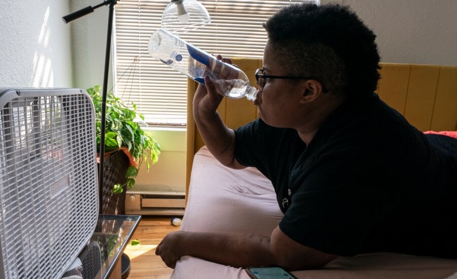 A person drinks water in front of a box fan while trying to stay cool in their apartment without air conditioning in Portland, Ore., on Thursday, Aug. 12, 2021.