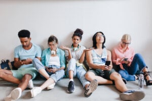 Tired international students sitting on the floor and using theis phones after lecture.