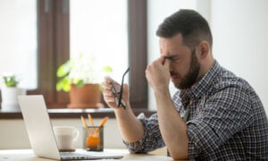 A stressed person rubbing his eyes while staring at laptop.