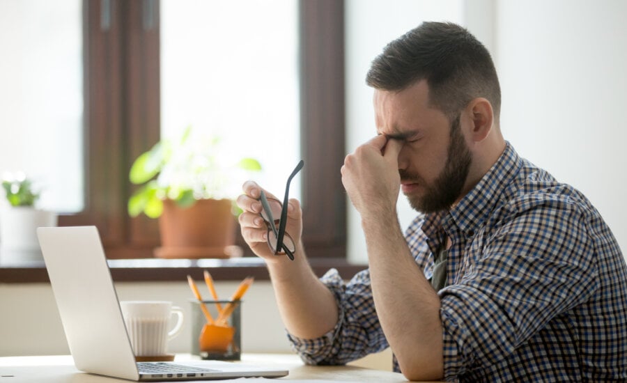 A stressed person rubbing his eyes while staring at laptop.