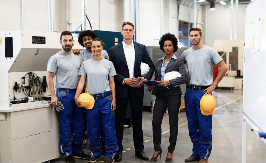 Portrait of group of engineers and corporate managers standing in a factory and looking at camera.