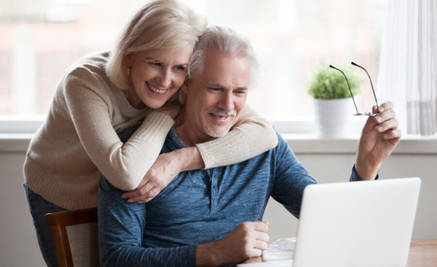 Senior middle aged happy couple embracing using laptop together, smiling elderly family reading news, shopping online at home, older people and computer or good vision after laser correction concept