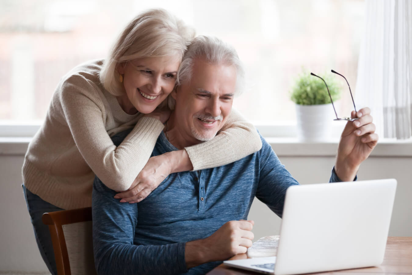 Senior middle aged happy couple embracing using laptop together, smiling elderly family reading news, shopping online at home, older people and computer or good vision after laser correction concept